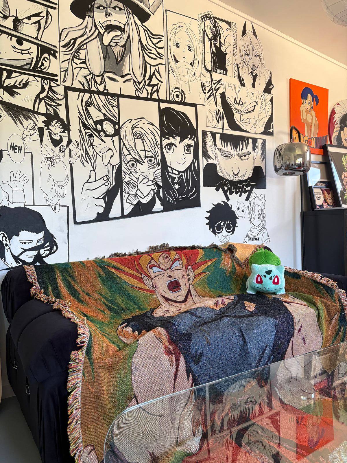A colorful woven throw blanket featuring an anime character design draped over a black sofa in a room with anime wall art.